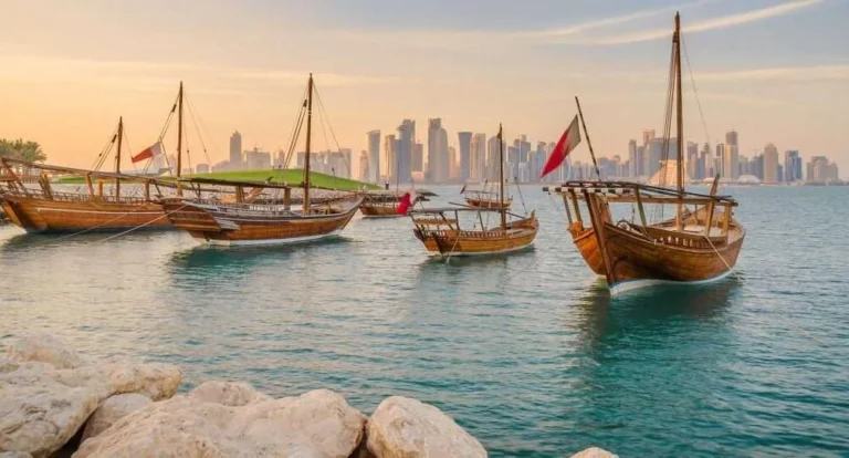 Traditional wooden boats float on calm blue water near a rocky shore, with a modern city skyline and tall skyscrapers in the background under a golden sky—capturing one of the best things to do in Doha.
