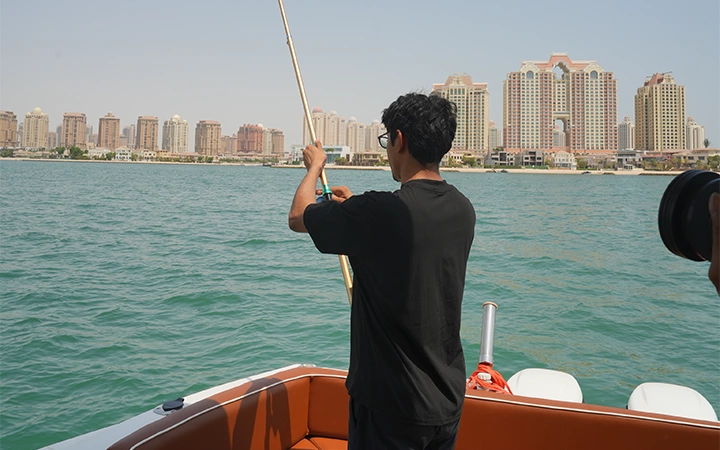 A person in a black shirt enjoys a Private Speed Boat Fishing Trip on calm water, with tall modern buildings rising in the background beneath a clear sky.