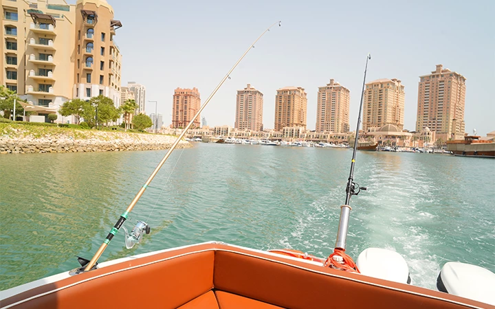 Enjoy a Private Speed Boat Fishing Trip, gliding on calm water with fishing rods ready, as you head toward a marina lined with tall, modern apartment buildings under a clear sky.