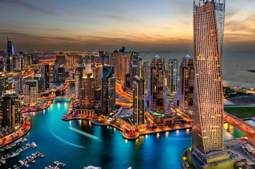 A vibrant cityscape at dusk with illuminated skyscrapers, winding waterways, and a marina filled with boats; the sky is a gradient of orange and blue as night falls over the ultimate incentive travel destination.