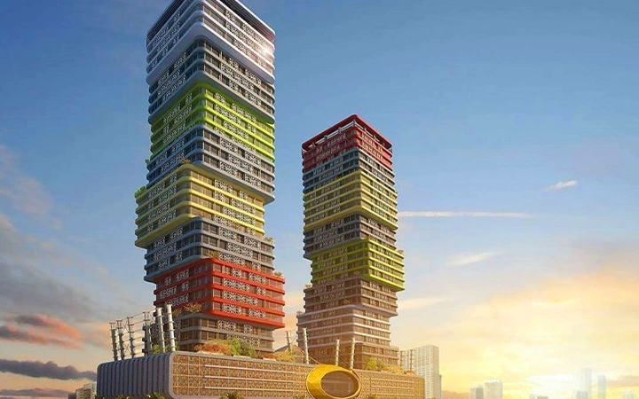 Two modern, multicolored high-rise buildings with stacked, offset rectangular sections stand against a blue sky at sunset—perfect to admire after a half day desert safari Qatar adventure. The base is patterned and features a central oval-shaped structure.