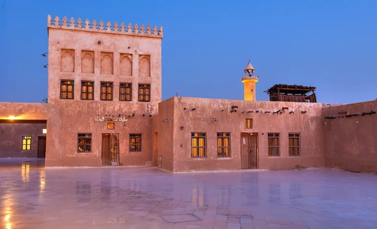 Traditional Qatari building with beige walls and arched windows, featuring a square tower with decorative crenellations—a must-see for anyone exploring the top 10 things to do in Qatar—photographed at dusk on a reflective courtyard.