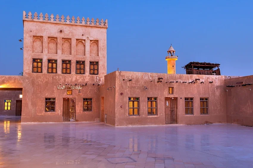 Traditional Qatari building with beige walls and arched windows, featuring a square tower with decorative crenellations—a must-see for anyone exploring the top 10 things to do in Qatar—photographed at dusk on a reflective courtyard.