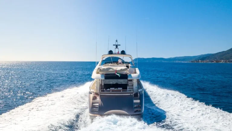 A luxury yacht speeds away on a clear blue sea, leaving white waves in its wake, with a distant coastline and mountains visible under a bright, sunny sky—echoing the allure of the best places to visit in Qatar.