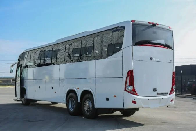 A large, modern white VIP Coach for Driver Qatar is parked on a paved surface under a clear blue sky, viewed from the rear left side.