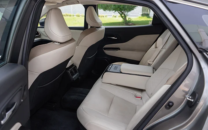 The image shows the backseat interior of a Toyota Camry Qatar with light beige leather seats, a fold-down center armrest, and black carpeting. The doors and front seats are visible, with sunlight coming through the windows.