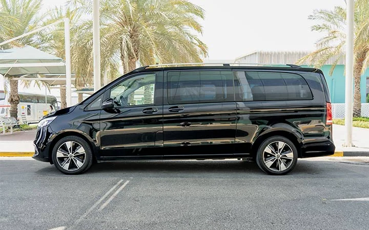 A black Mercedes Viano in Qatar with tinted windows is parked on a street, set against palm trees and modern buildings in the background.