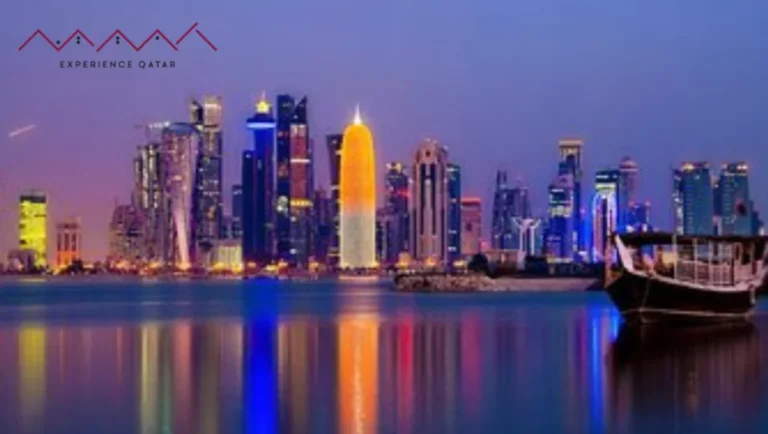 A vibrant night view of Doha’s illuminated skyline reflecting on the water, with a traditional dhow boat in the foreground—perfect for unforgettable Shore Excursions. The Experience Qatar logo is in the top left corner.