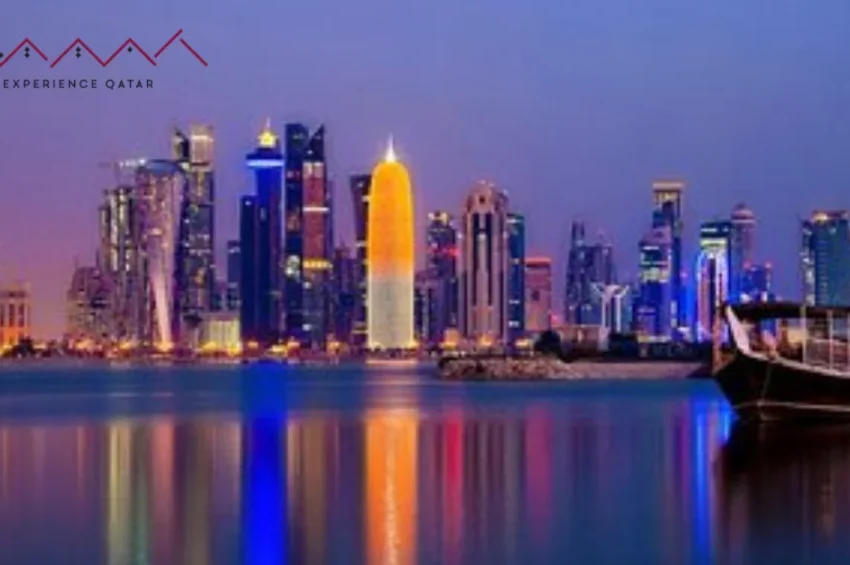 A vibrant night view of Doha’s illuminated skyline reflecting on the water, with a traditional dhow boat in the foreground—perfect for unforgettable Shore Excursions. The Experience Qatar logo is in the top left corner.