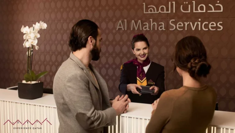 A man and woman stand at a reception desk, speaking with a smiling female staff member in uniform. The backdrop displays Al Maha Services in English and Arabic, highlighting their commitment to exceptional hospitality. A white orchid is on the counter.