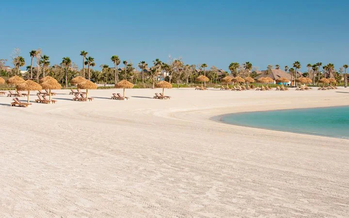 Golden sandy shoreline with palm trees and umbrellas at Banana Island Beach Doha