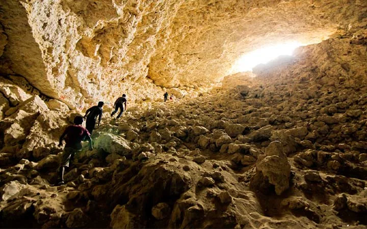 Visitors hiking inside Dahl Misfar Cave Qatar with rocky formations and sunlight