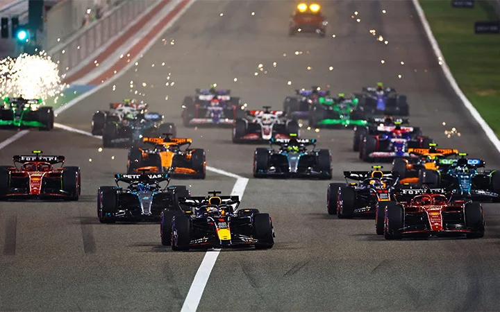 A group of Formula 1 cars race down the track at high speed, sparks flying from one car in the background, during an electrifying nighttime Formula 1 Qatar event.