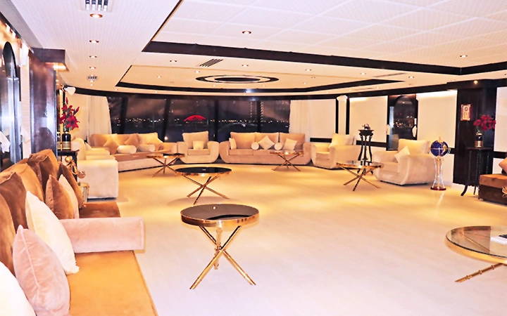 A spacious, modern lounge aboard the Wave Private Houseboat features cream-colored sofas, gold and glass coffee tables, large windows, soft lighting, and decorative accents for an elegant and inviting atmosphere.