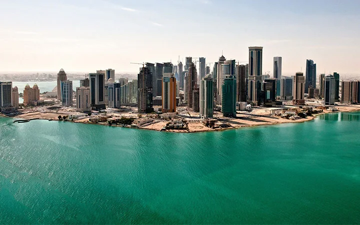 A panoramic view of a modern city skyline with tall skyscrapers along the coastline, bordered by the turquoise waters of West Bay Beach and clear skies above.