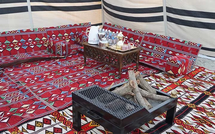 Traditional Arabic tent interior with colorful patterned carpets and cushions, a low wooden table with tea and coffee sets, and a metal fire pit—perfect for an authentic Private Beach Setup in Qatar.