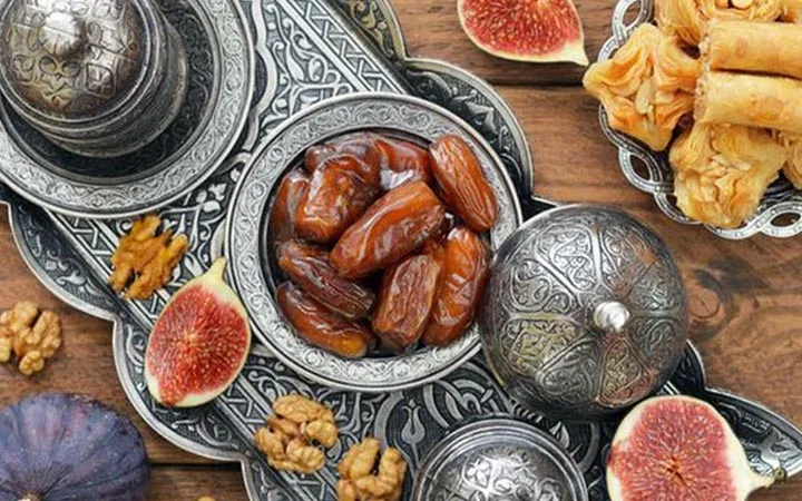 Ornate silver dishes with dates, figs, walnuts, and pastry pieces arranged on a wooden surface, perfect for a traditional Group Iftar with Private Set-up showcasing Middle Eastern snacks.