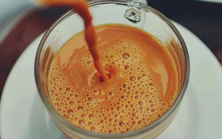 A close-up view of chai being poured into a glass cup, forming bubbles on the surface. The cup, set on a white saucer, evokes cozy moments—perfect after a Ramadan 5K Walk and Karak With Guided Tour.