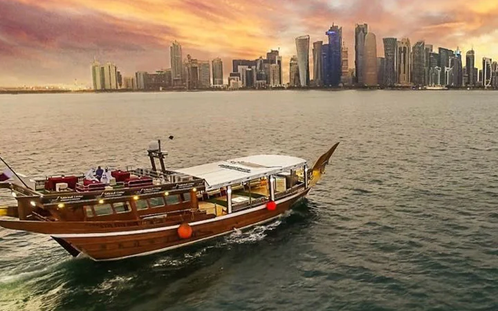Traditional dhow boat sailing Doha waters with sunset city skyline view