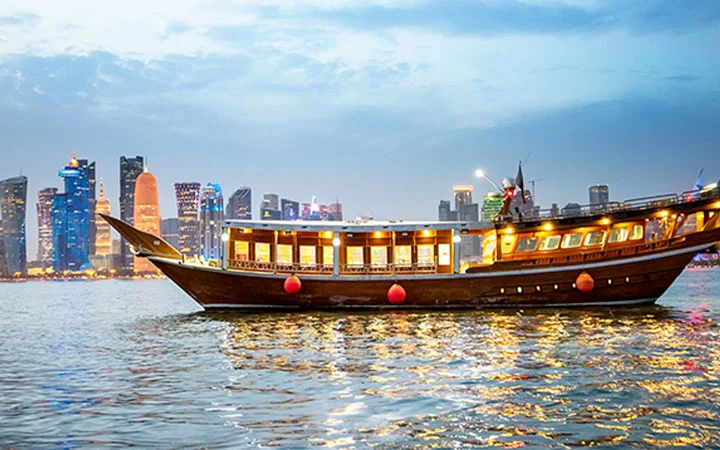 Wooden dhow boat sailing against Doha skyline during sunset