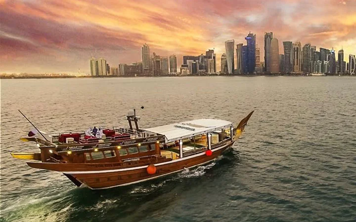 A traditional wooden boat sails on calm water at sunset during Eid-Swim, with a modern city skyline featuring tall skyscrapers in the background and a colorful sky above, capturing the spirit of celebration and the joy to jump into festivities.