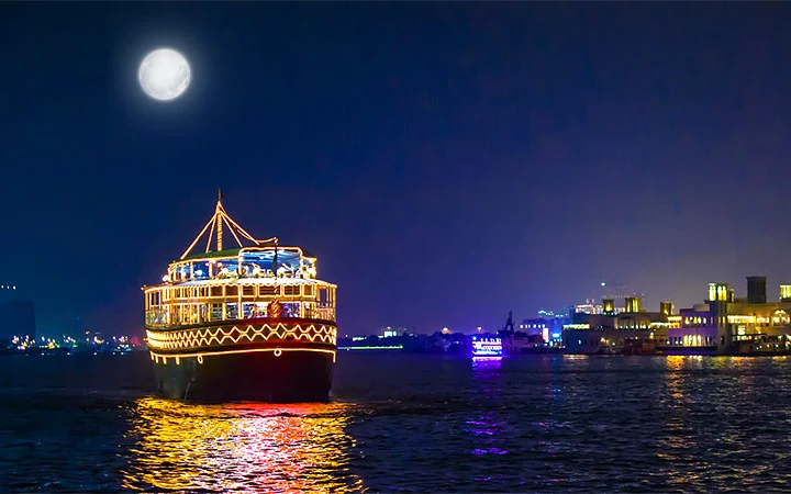Traditional dhow lit under full moon during Doha evening cruise
