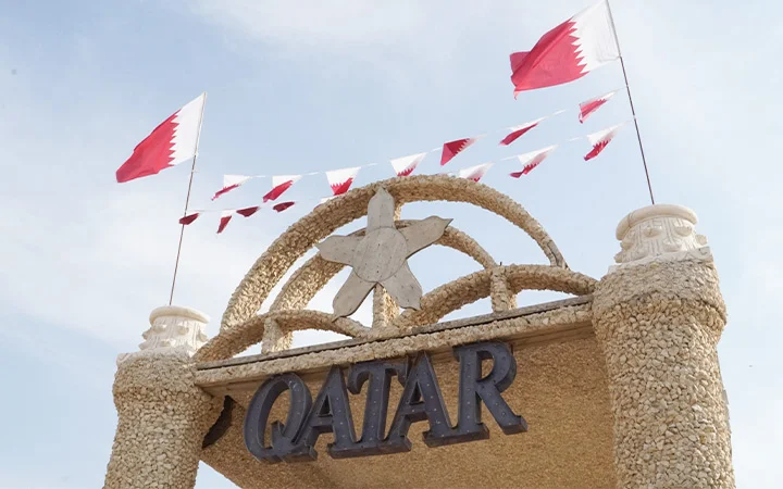 Stone arch entrance with Qatar flags at Ain Mohamed Village Qatar