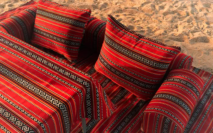 Traditional red and black patterned Arabic cushions and seating arranged on sand, creating a cozy, inviting outdoor setting—perfect for relaxing after a day trip to Safliyah Island from Doha.