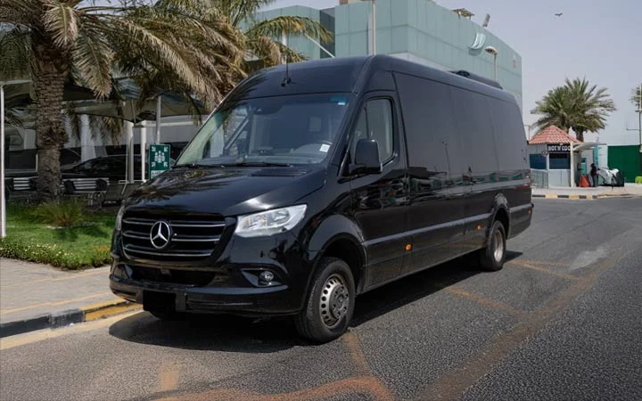 A black Mercedes Sprinter VIP Bus is parked on a city street in Doha, near palm trees and modern buildings under a clear sky.